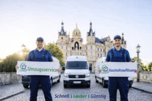 Zwei Umzugshelfer in blauen Uniformen stehen vor Lieferwagen und einem historischen Gebäude und halten Schilder mit den Aufschriften Umzugsservice, Haushaltsauflösung und Entrümpelung.